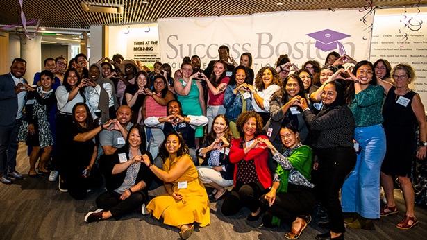 A group of people pose for a photo in front of a large Success Boston sign.