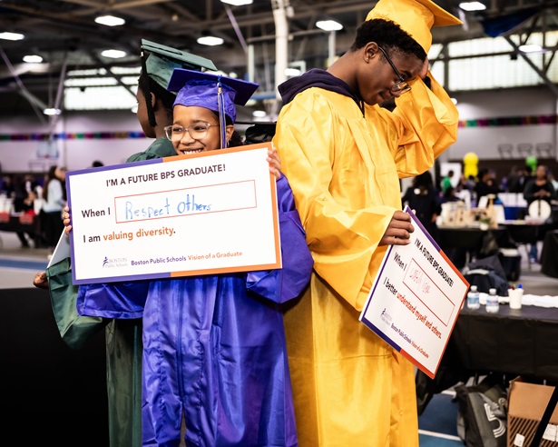 A group of young students wear graduation caps and gowns, they are holding signs that say "I'm a future BPS graduate! Boston Public Schools Vision of a Graduate"